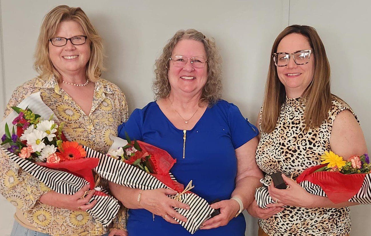 three women standing together holding flowers at employee awards banquet